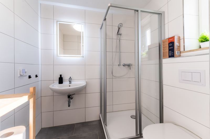Badezimmer mit Dusche, Waschbecken und beleuchtetem Spiegel